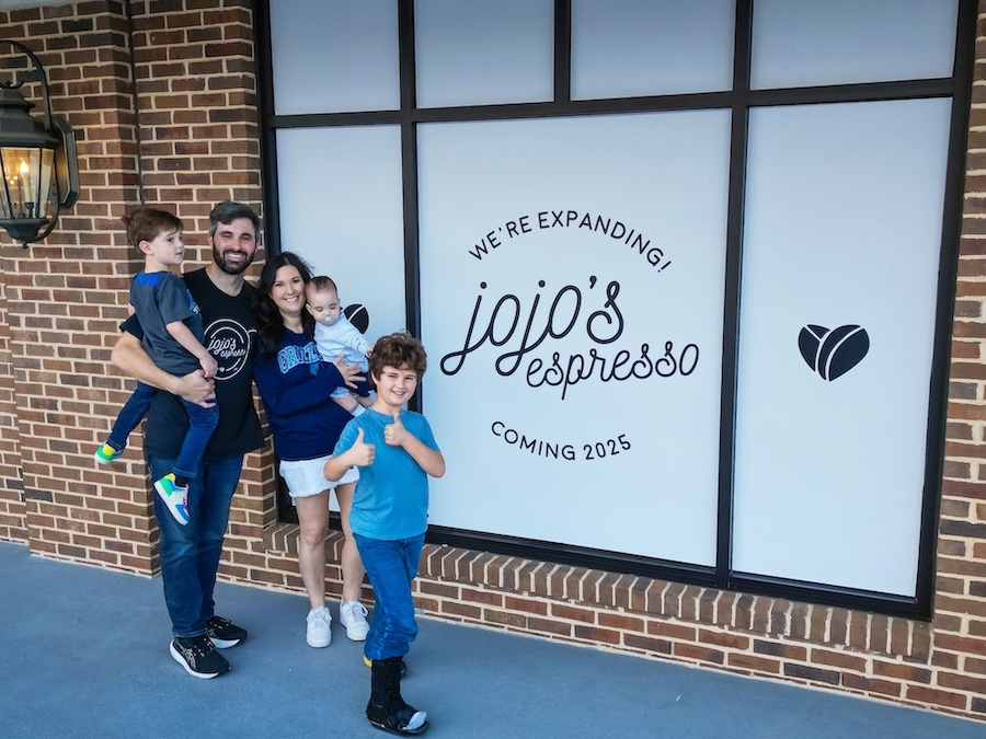 Family standing in front of a window with signage for "jojo's espresso" expansion, coming 2025.