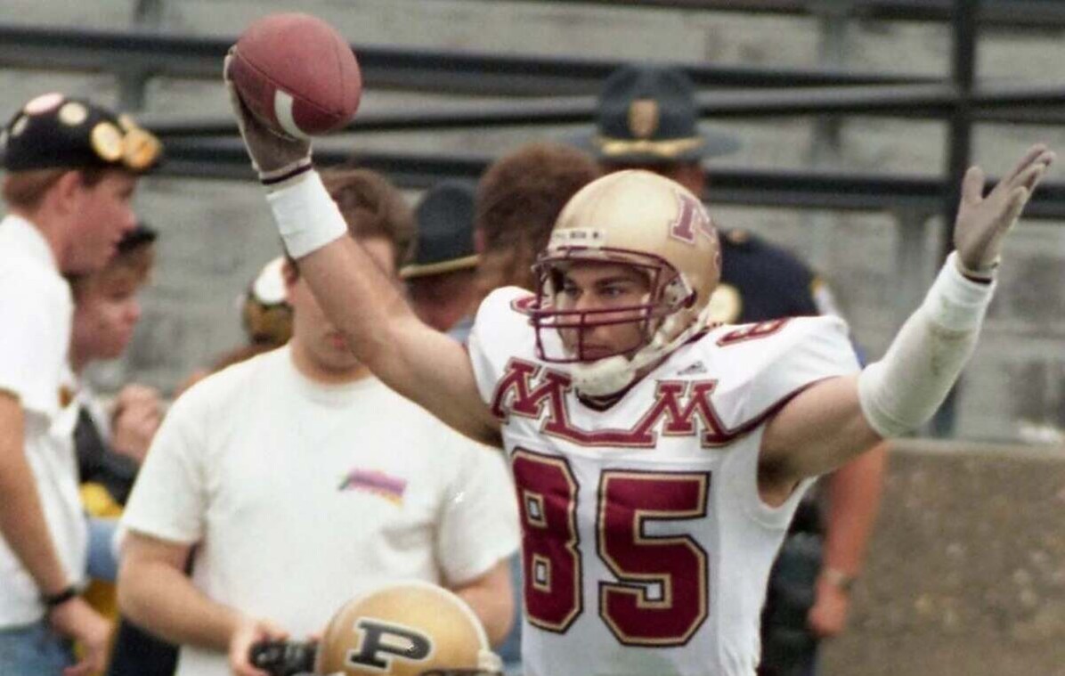 University of Minnesota football player wearing number 85 raises a football in one hand and gestures with the other.