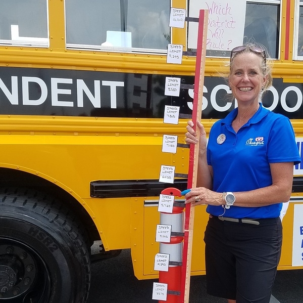 Woman holding a red pole with labels next to a yellow school bus.