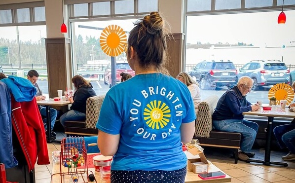 Person in a blue T-shirt with sun design and text  reading "You brighten our day."