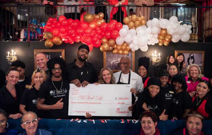 A group of people holding a large ceremonial check for $350,000 in front of red, white, and gold balloons.