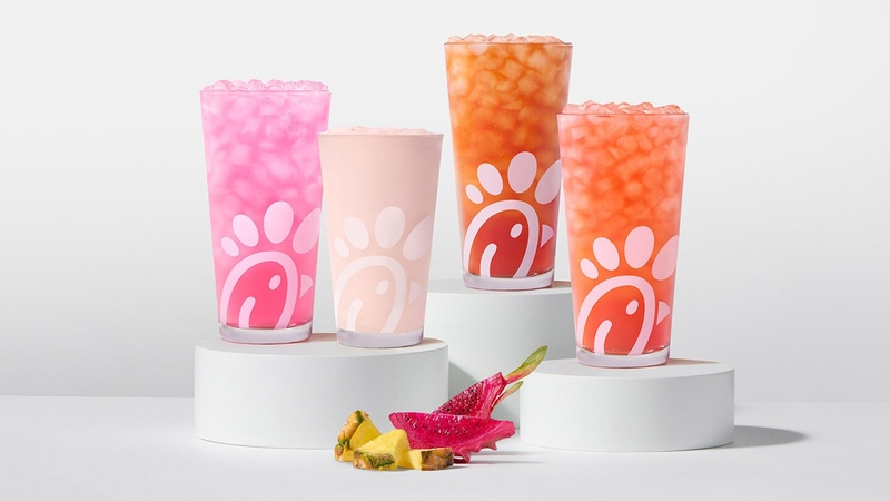 A glass of a Pineapple Dragonfruit Lemonade, Frosted Lemonade, Iced Tea and Sunjoy on risers with pieces of pineapple and dragonfruit next to them