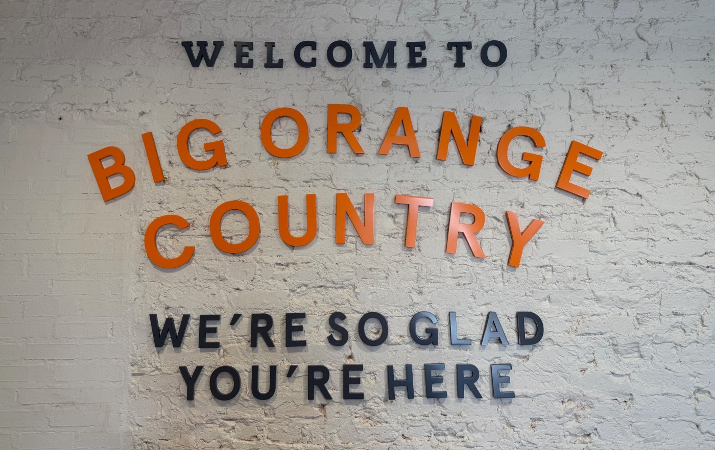 Text on a brick wall reads, "WELCOME TO BIG ORANGE COUNTRY. WE’RE SO GLAD YOU’RE HERE."