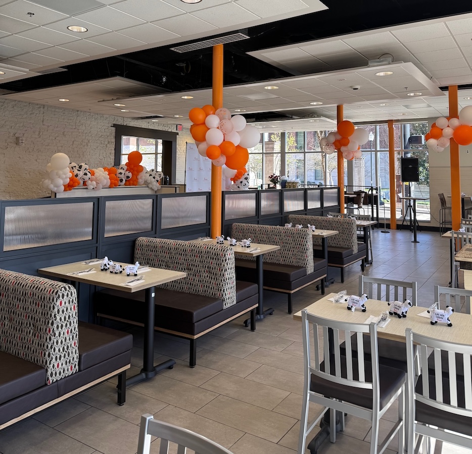 Interior of restaurant with booths and tables, decorated with orange and white balloons and toy cows.