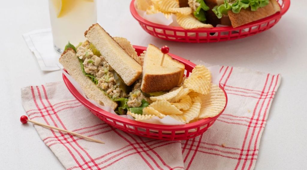 A chicken salad sandwich with potato chips in a red basket