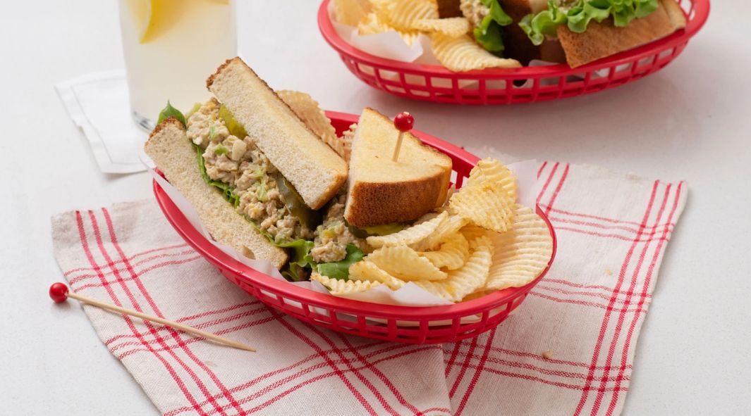 A chicken salad sandwich with potato chips in a red basket