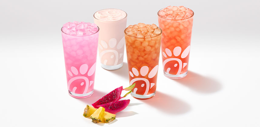 A glass of a Pineapple Dragonfruit Lemonade, Frosted Lemonade, Iced Tea and Sunjoy with pieces of pineapple and dragonfruit next to them on a gray background