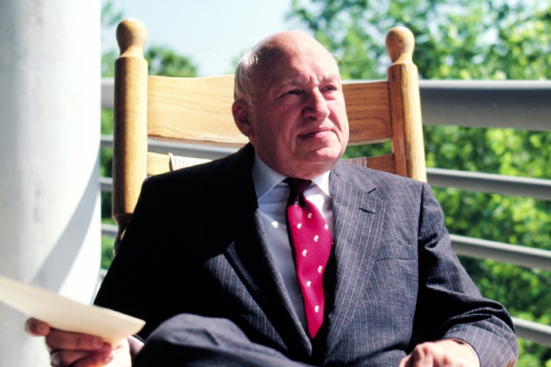 S. Truett Cathy sitting in a rocking chair outside and holding a paper