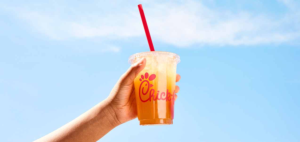 A customer holding a cup of Chick-fil-A Iced Tea against a bright blue sky.