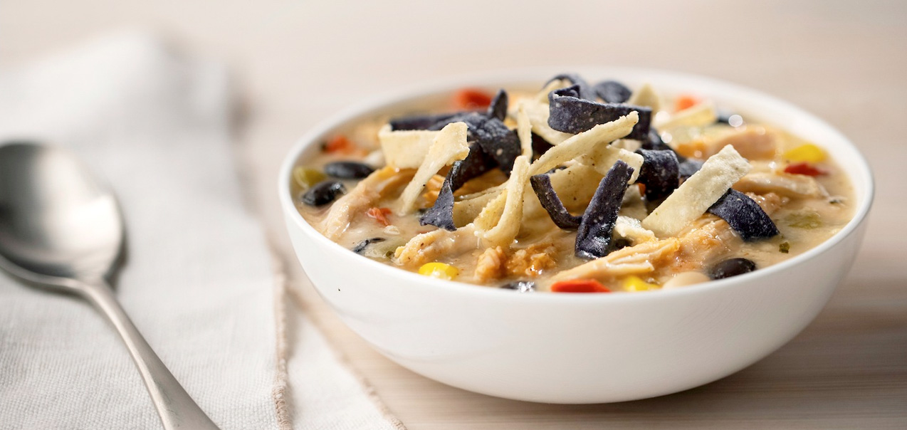 A bowl of Chicken Tortilla Soup next to a linen napkin and spoon