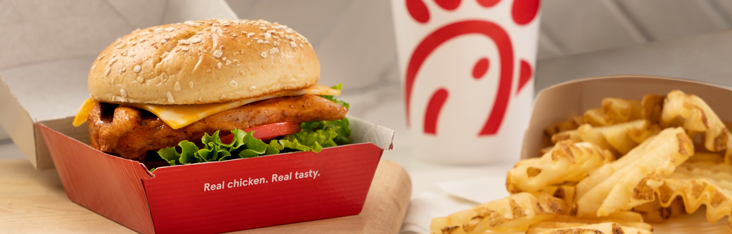 Chick-fil-A sandwich in a box that says "Real chicken. Real tasty." with waffle fries and a drink.