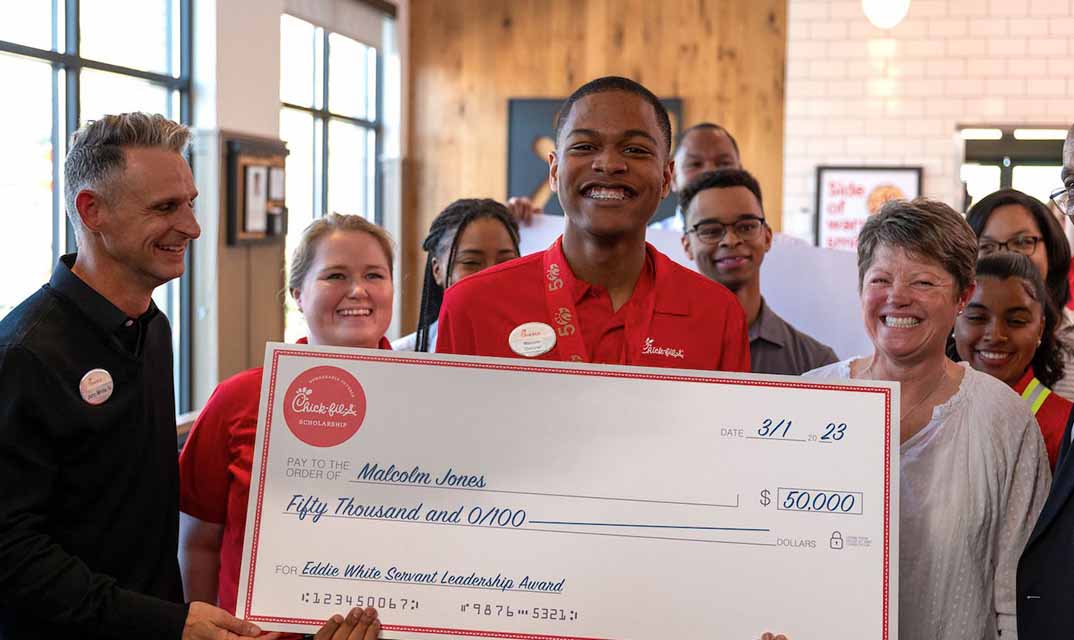 Eddie holds a large Chick-fil-A scholarship check while smiling surrounded by team members.