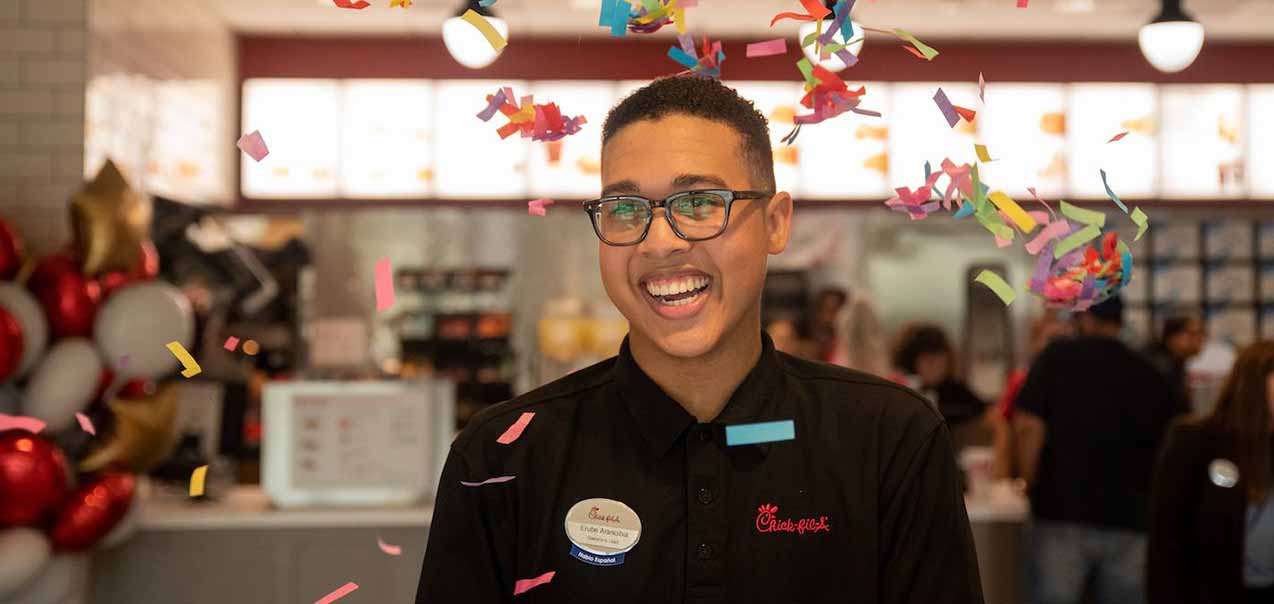 Team member smiling inside of Chick-fil-A as confetti falls.