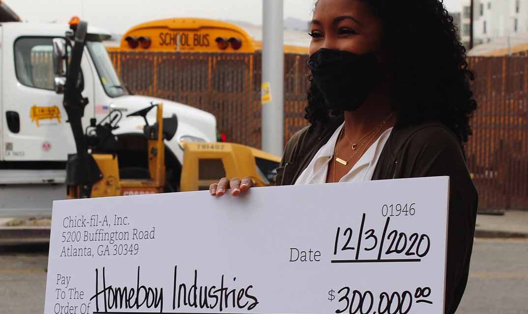 A woman smiles holding an oversized check made out to Homeboy Industries.