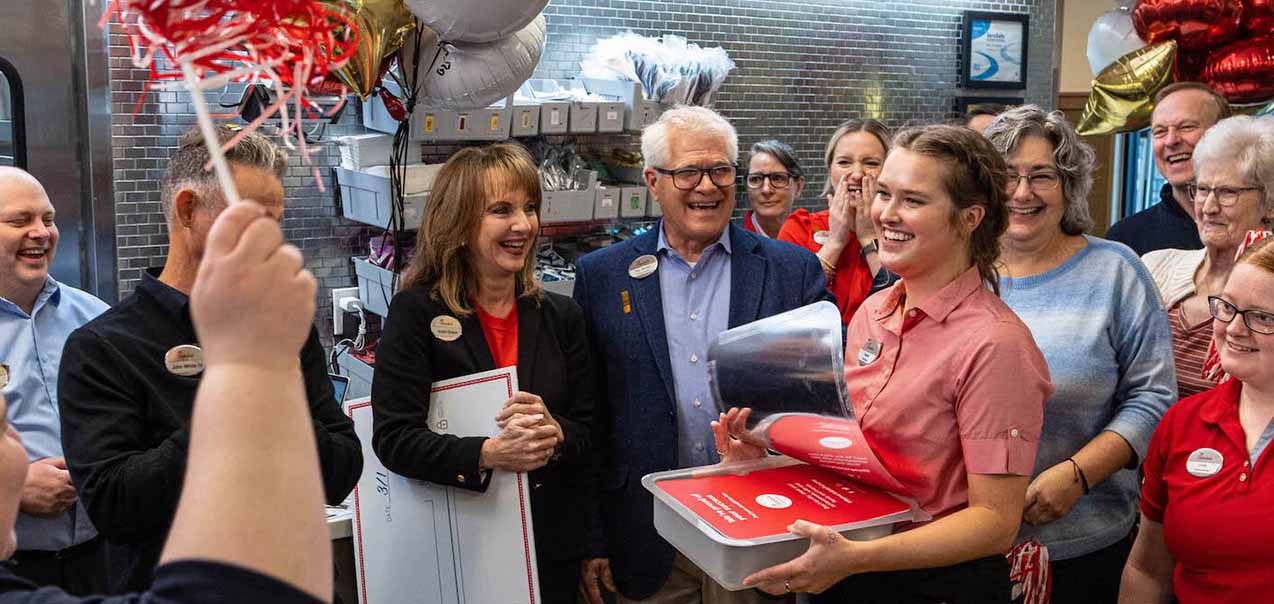 A Chick-fil-A Leadership Scholar and team members pose with red award plaque with colorful balloons.