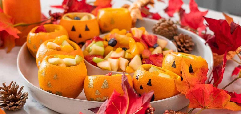 Oranges decorated to look like carved pumpkins filled with fruit.