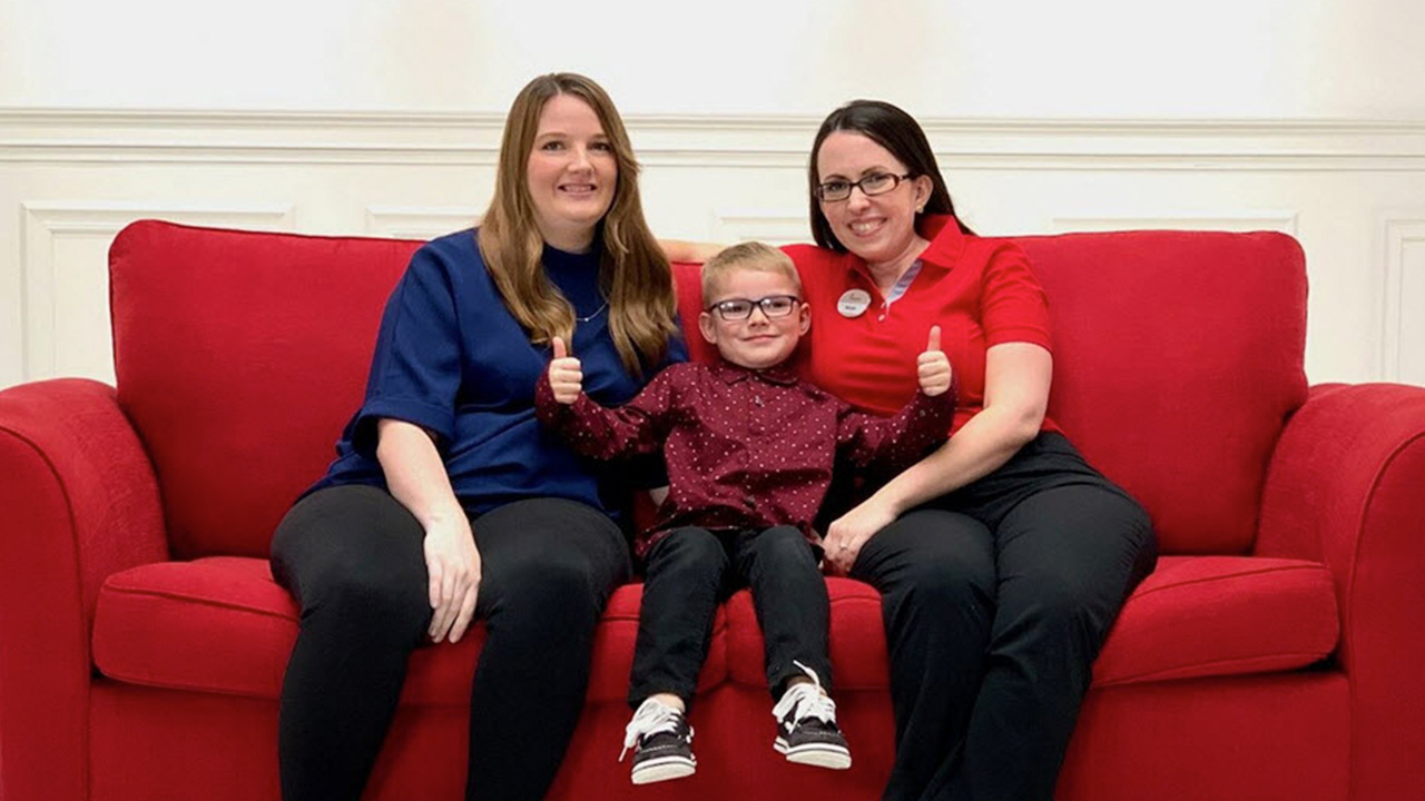 A young customer and his mom sit on a red couch next to a Chick-fil-A employee.