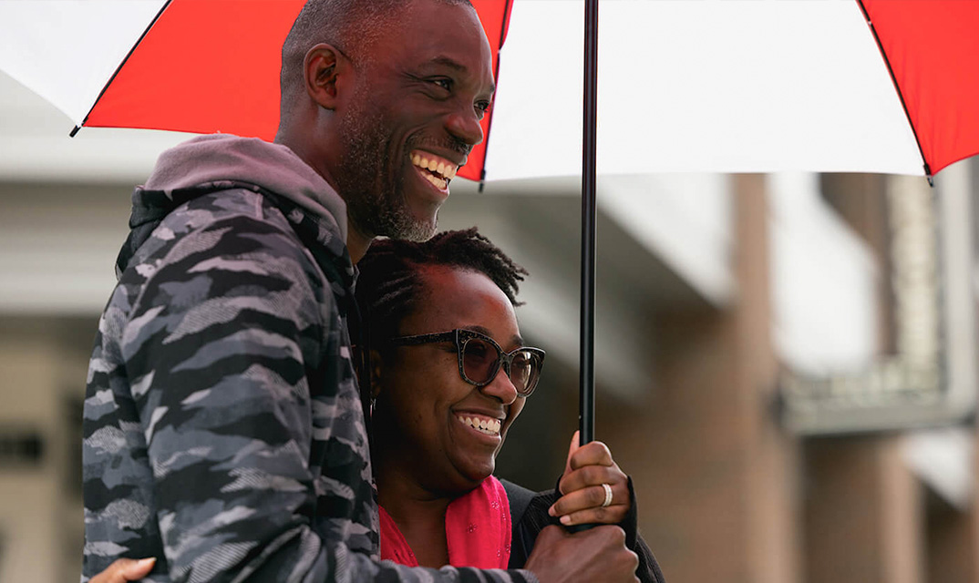 Two people smile while sharing a red and white umbrella