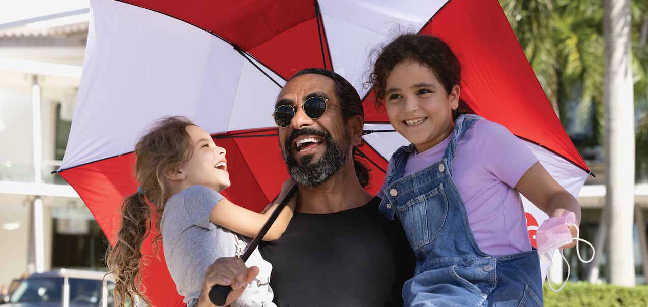 Man holding his two daughters while also holding a large red and white umbrella