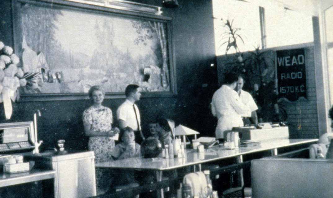 Diner interior scene with people, a scenic mural, and a "WEAD Radio 1570 KC" sign.