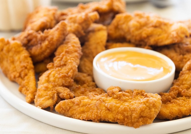 Chick-n-Strips on a platter with a cup of honey mustard sauce