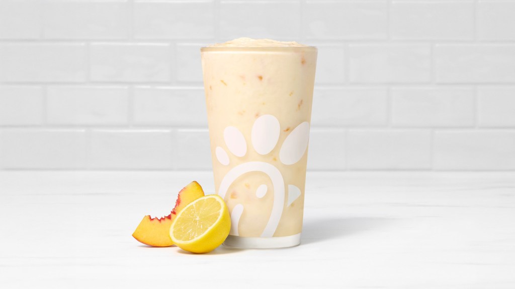 Peach Frosted Lemonade in a glass accompanied by a peach and a lemon slice.