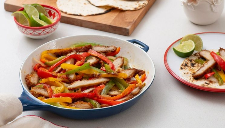 Chicken Fajitas in a skillet with a side of limes and tortillas