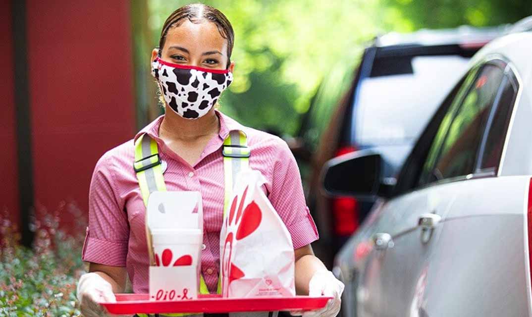A Chick-fil-A Team member brings food out to a car in the drive-thru
