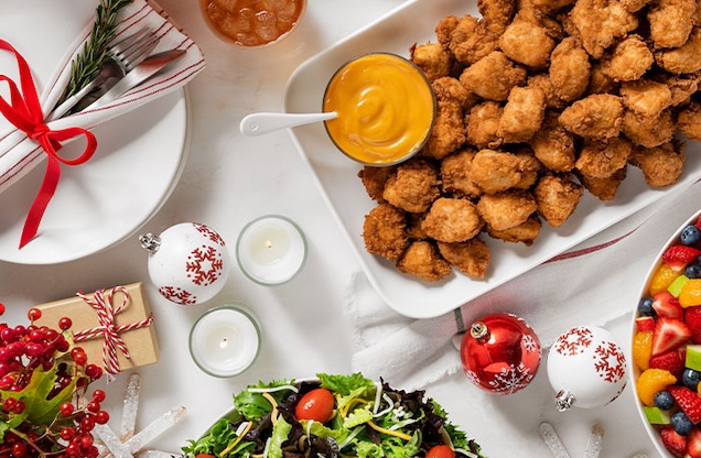 A festive table spread with nuggets, fruit salad, mixed greens, and holiday decorations.
