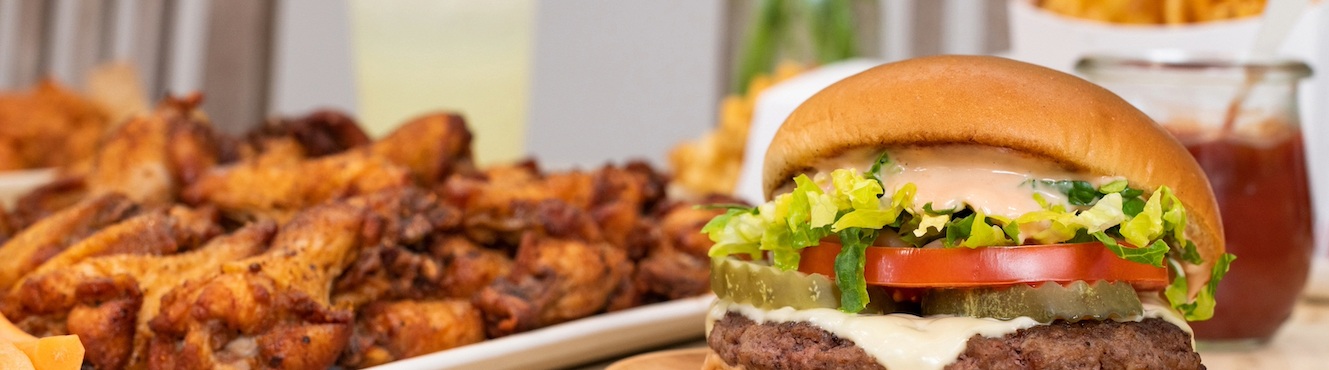 A burger with toppings, wings and waffle fries