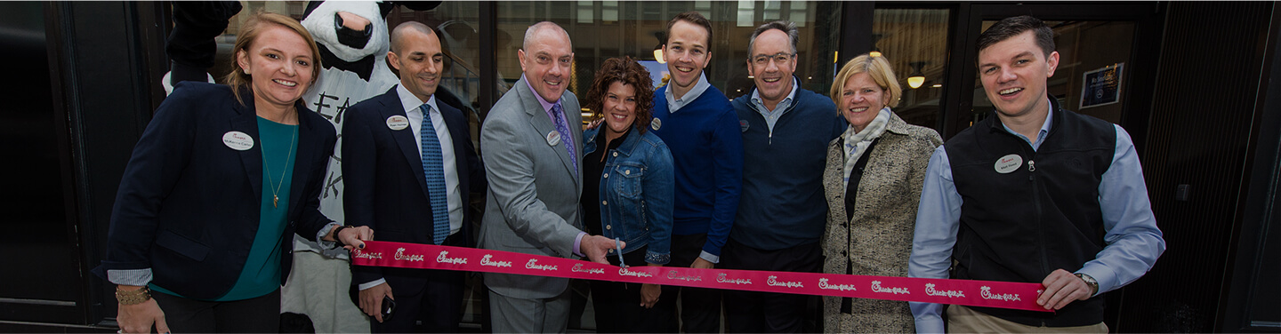 A group of people at a ribbon-cutting ceremony holding a red "Chick-fil-A" ribbon.