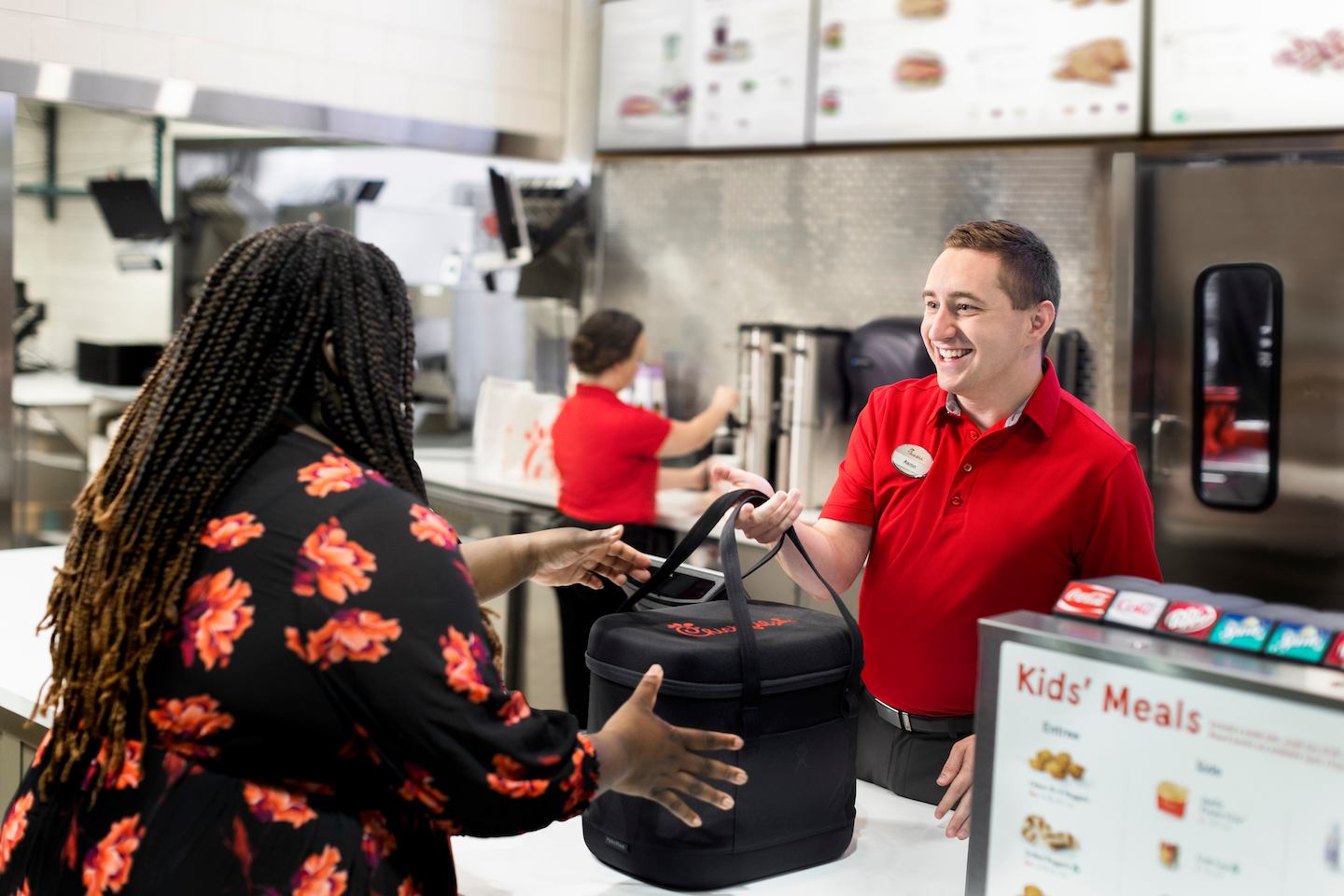 A Team Member smiling and handing a Customer an insulated Chick-fil-A bag