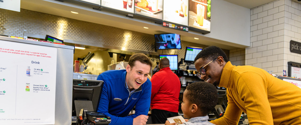 A child and an adult interacting with a smiling Chick-fil-A employee at the counter.