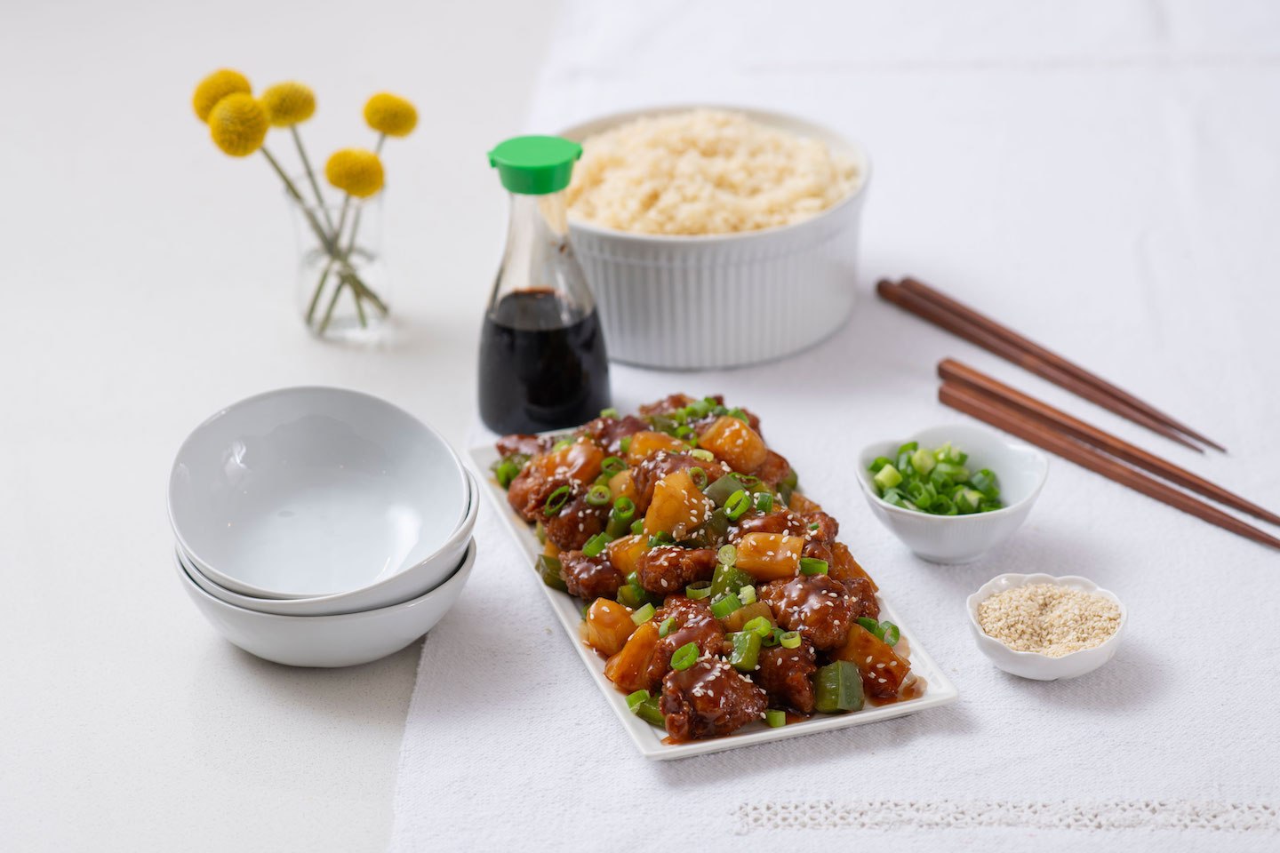 Rectangular plate of glazed chicken with vegetables, garnished with green onions and sesame seeds, alongside small dishes with green onions and sesame seeds.
