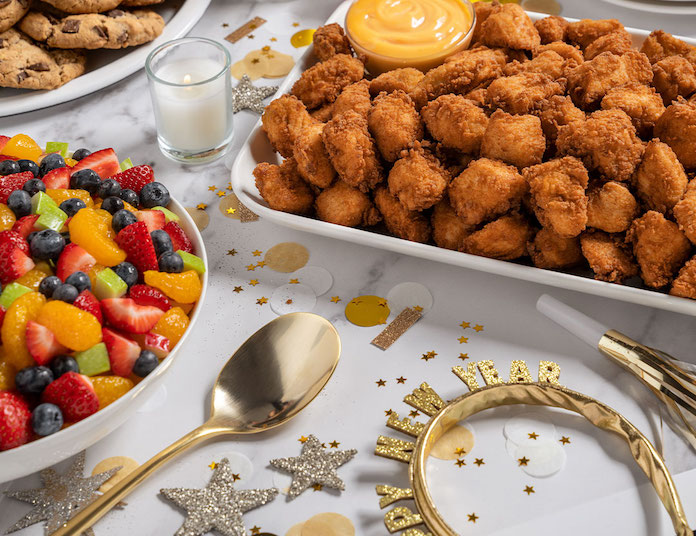A festive table setting with chicken nuggets, fruit salad, and New Years decorations.