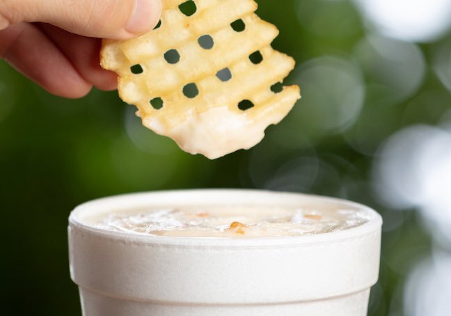 A waffle fry being dipped into a peach milkshake
