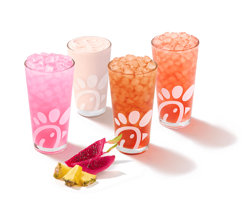 A glass of a Pineapple Dragonfruit Lemonade, Frosted Lemonade, Iced Tea and Sunjoy with pieces of pineapple and dragonfruit next to them on a gray background