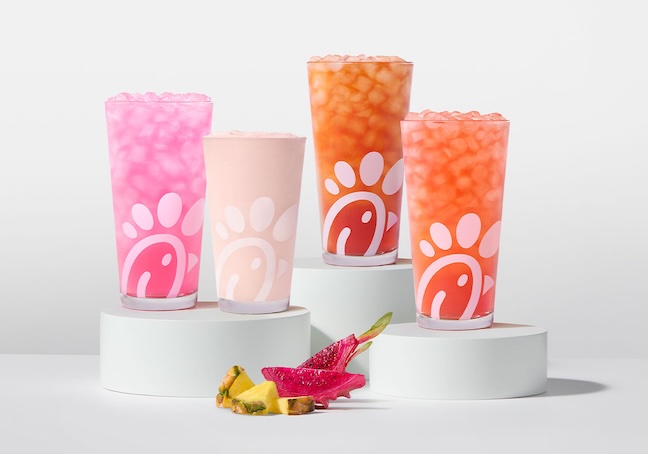 A glass of a Pineapple Dragonfruit Lemonade, Frosted Lemonade, Iced Tea and Sunjoy on risers with pieces of pineapple and dragonfruit next to them