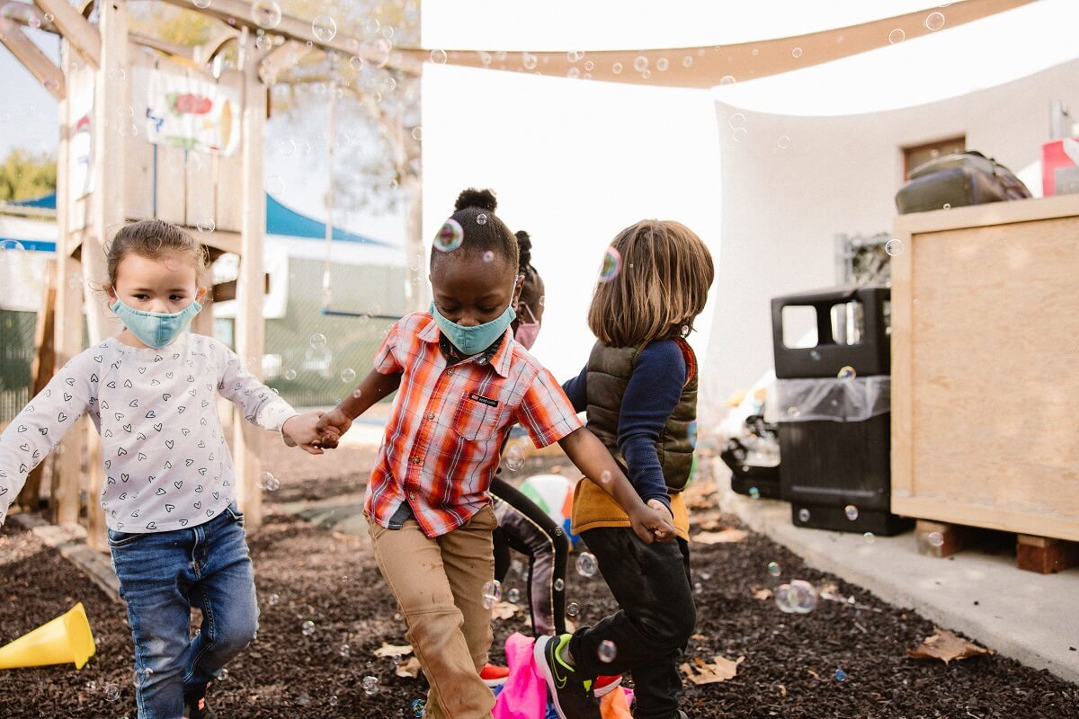 Four preschoolers hold hands while playing in bubbles