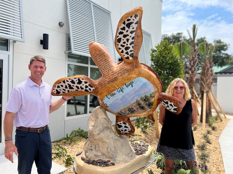 Two people pose with a Colorful sea turtle sculpture.