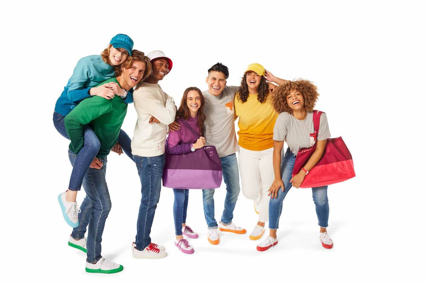 A group of seven people posing joyfully in casual colorful clothing against a white background.