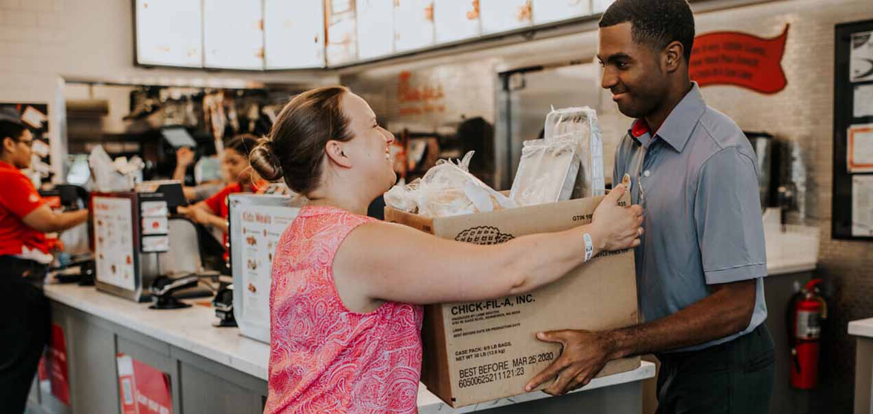 A Team Member smiling and handing a Customer a large box of food