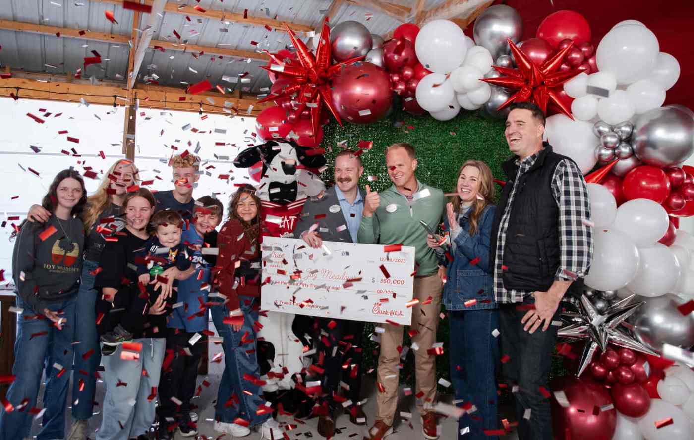 A group of Chick-fil-A team members celebrate indoors with pom-poms, balloons, and streamers as one person holds a large check.