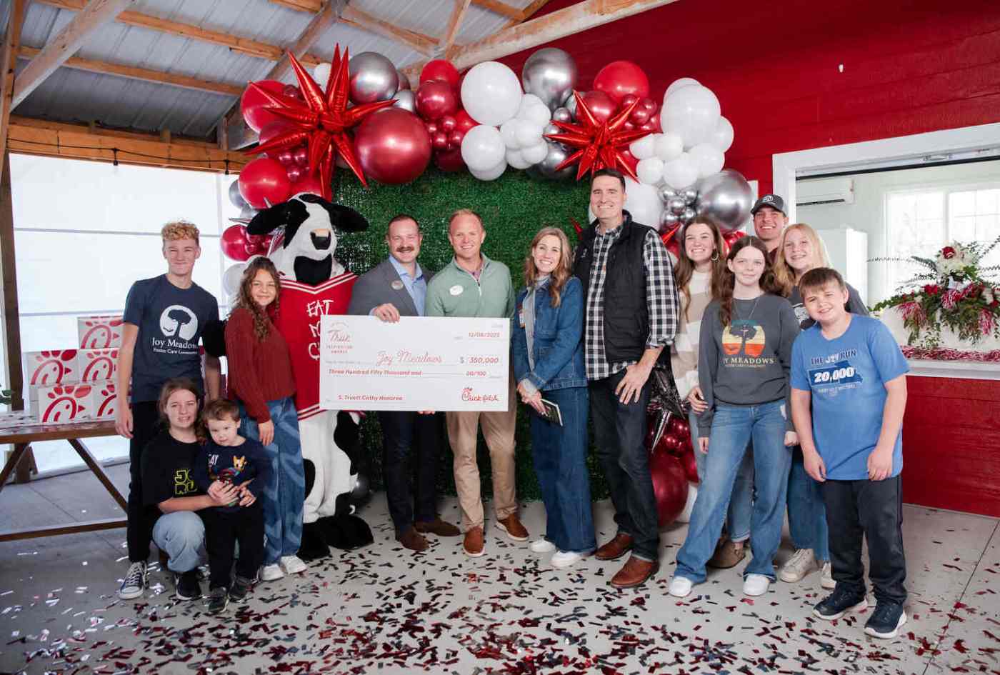A group of people and the Chick-fil-A mascot holding a large check with balloons in the background.