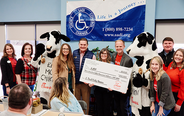 Group of people standing in front of the ADI nonprofit sign, holding a large check from Chick-fil-A®