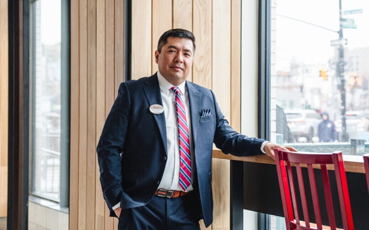 Person in a navy suit beside a window in a bright, wood-paneled interior of a Chick-fil-A location