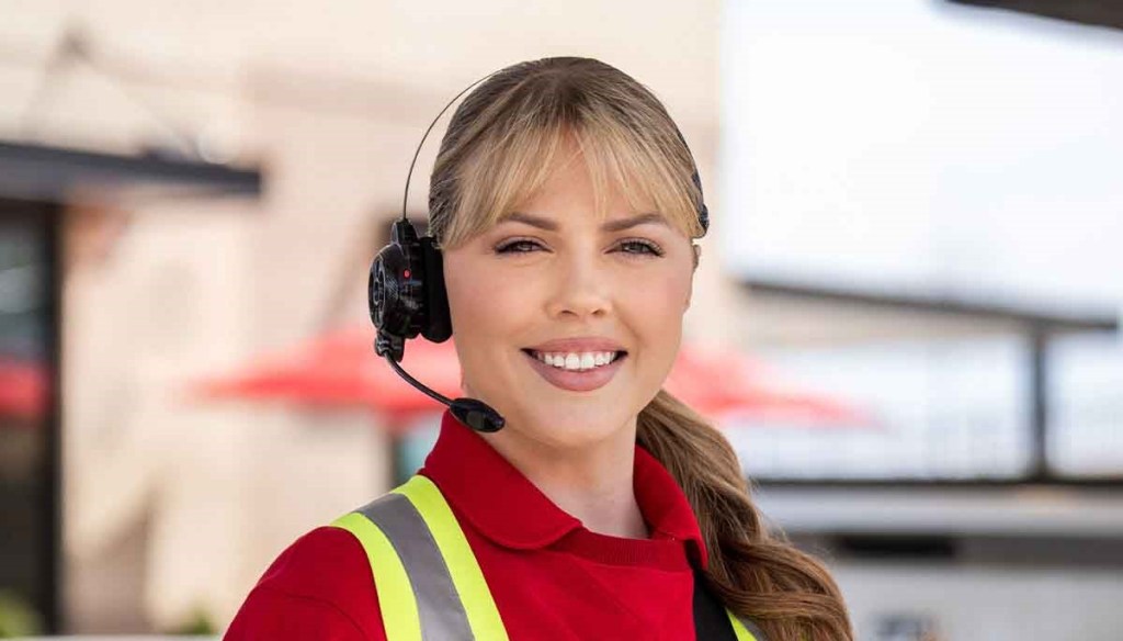 A Team Member wearing a safety vest and headset standing outside a Chick-fil-A Restaurant