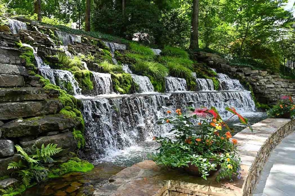 Cascading waterfall over stone terraces with green moss and vibrant flowers.