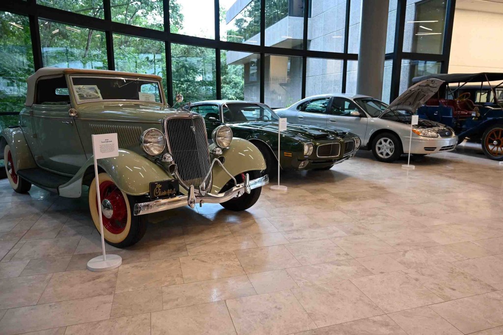 A display of vintage and modern cars inside a building with large windows.

