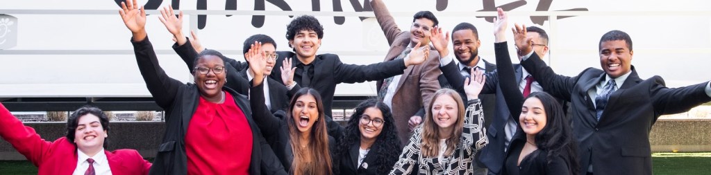 A group of Community Scholars in business attire celebrating with raised arms.